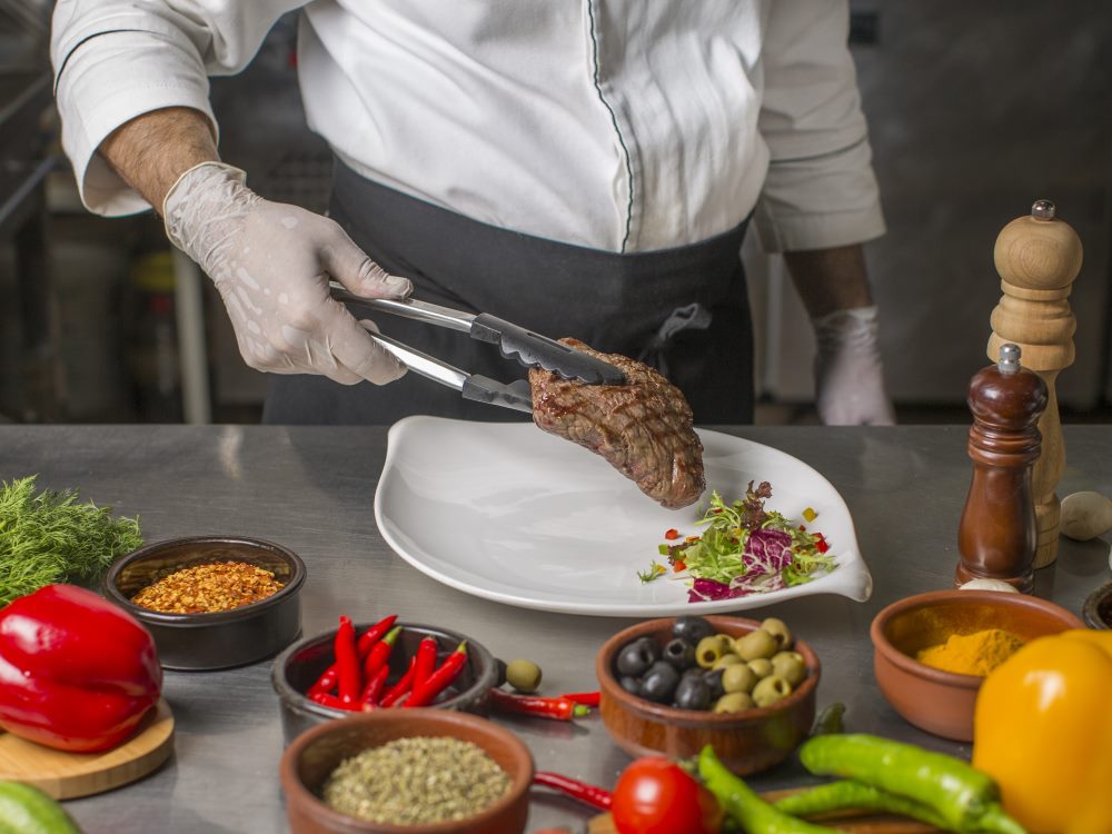 chef-putting-grilled-steak-serving-plate-with-herbs-salad