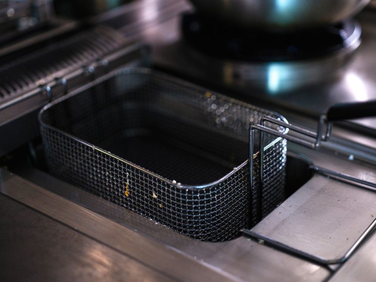A service technician carefully scrubs heavy black carbon deposits off the heating element of a commercial deep fryer in