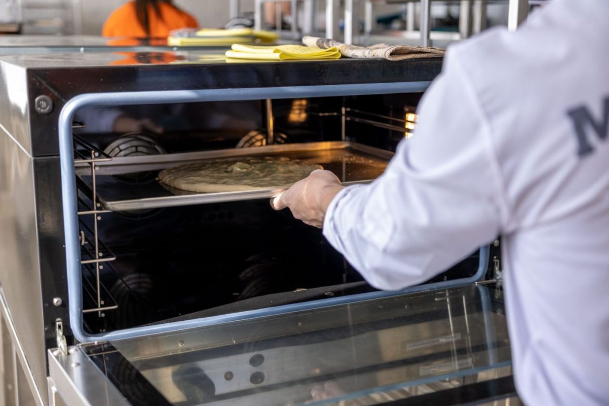 A chef opens a combi oven in a bright restaurant kitchen, with steam rising and trays of food inside.