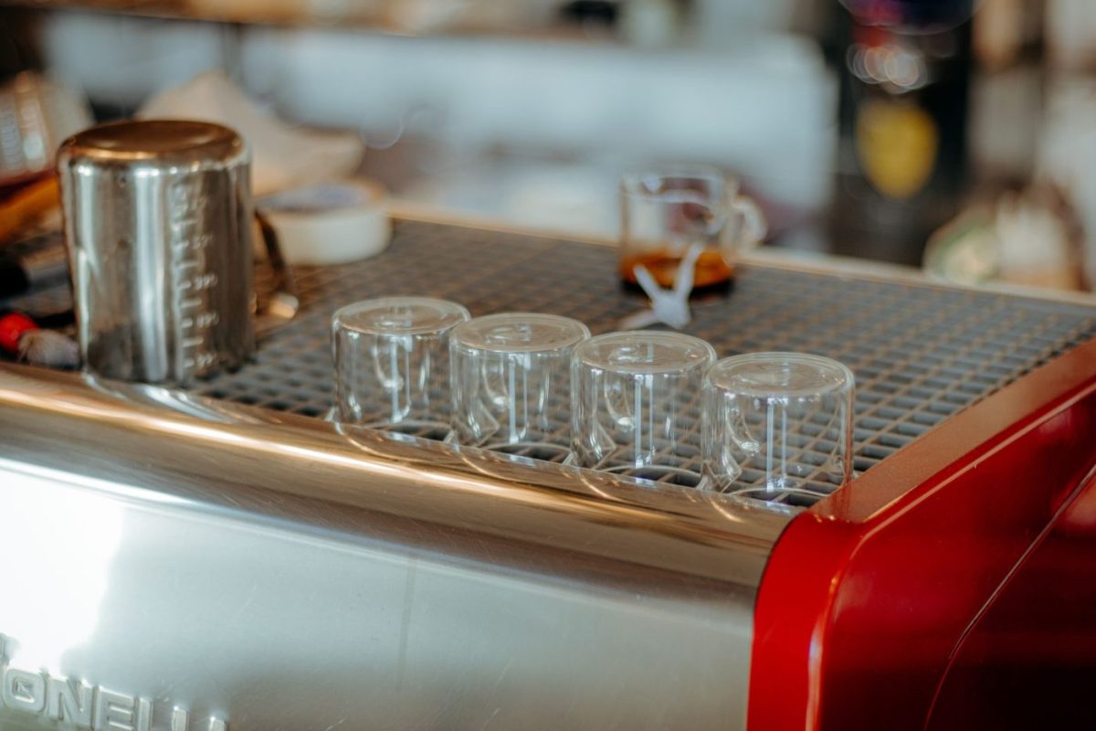 A commercial dishwasher washing glasses and plates in a busy cafe kitchen.