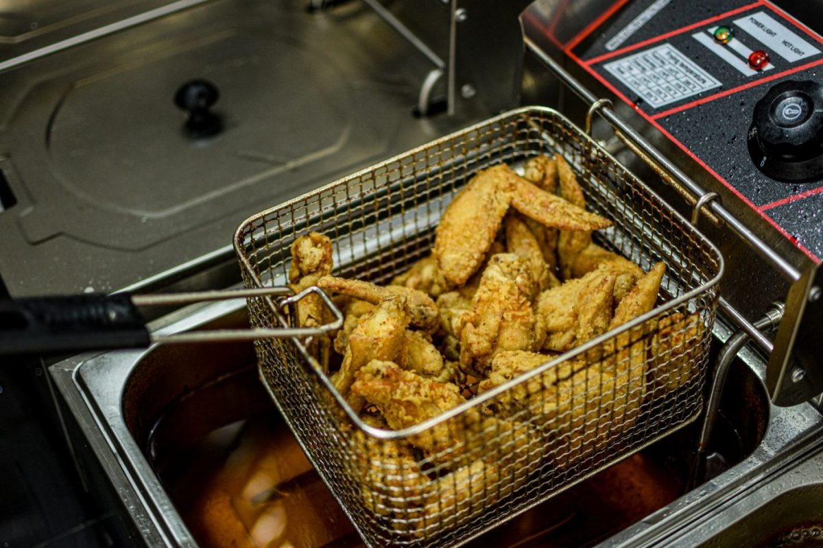 A restaurant worker filters and stores frying oil in a deep fryer inside a clean commercial kitchen.