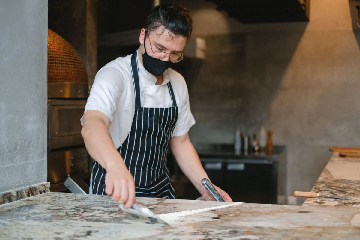 A chef in an apron wiping the inside of a combi oven cavity in a professional kitchen