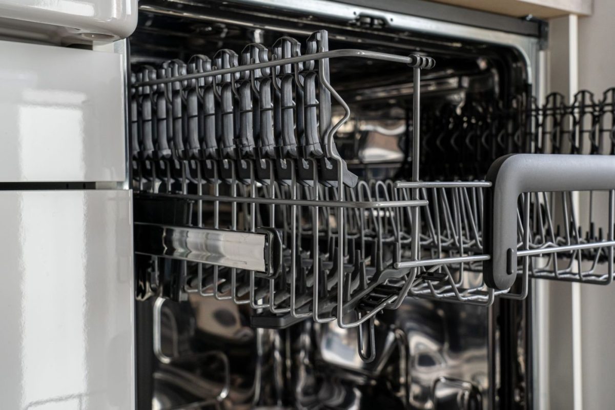 A person loads a dishwasher in a bright residential kitchen while noticing white residue on clean glassware.